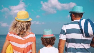 Kumsalda mutlu bir aile. İnsanlar yaz tatilinde eğleniyor. Baba, anne ve çocuk mavi deniz ve gökyüzü arka planına karşı. Tatil seyahati kavramı