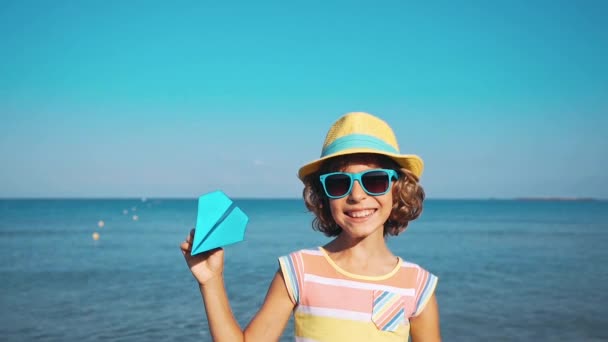 海と空の背景に紙飛行機で遊んで幸せな子 屋外の楽しい時を過す子供パイロット 夏のバケーション 旅行のコンセプトです 自由と想像力 — ストック動画