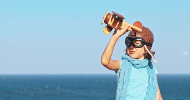 海と空の背景に対しておもちゃの飛行機で遊んで幸せな子 屋外の楽しい時を過す子供パイロット 夏のバケーション 旅行のコンセプトです 自由と想像力 — ストック動画