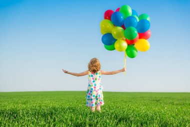 Parlak çok renkli balonlar açık oynayan mutlu çocuk. Çocuk mavi gökyüzü arka plan yeşil bahar alandaki eğleniyor. Sağlıklı ve aktif yaşam tarzı kavramı. Arkadan Görünüş