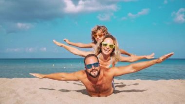 Kumsalda mutlu bir aile. İnsanlar yaz tatilinde eğleniyor. Baba, anne ve çocuk mavi deniz ve gökyüzü arka planına karşı. Tatil seyahati kavramı