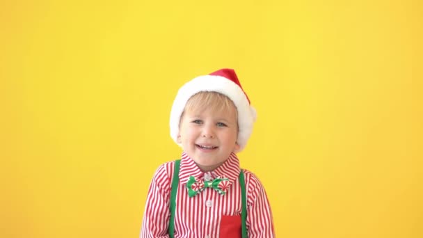 快乐的孩子戴着圣诞老人的帽子在黄色的背景 有趣的孩子竖起大拇指 圣诞节寒假概念 — 图库视频影像