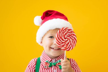 Sarı arka plan aleyhine elinde lolipop tutan mutlu çocuk