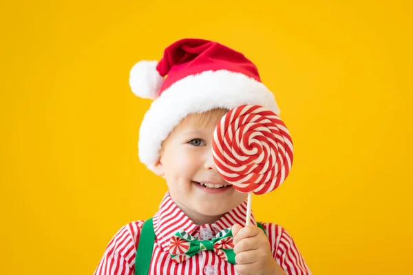 Happy child holding lollipop in hand against yellow background — Stock Photo, Image