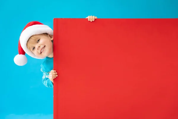 Criança feliz segurando banner de Natal vermelho em branco contra costas azuis — Fotografia de Stock