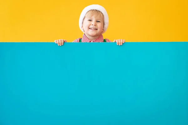 Niño feliz sosteniendo banner azul de Navidad en blanco contra amarillo b — Foto de Stock