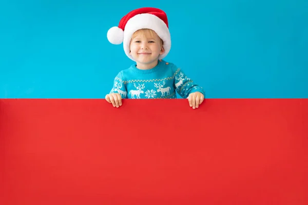 Felice bambino che tiene il banner rosso di Natale vuoto contro la schiena blu — Foto Stock