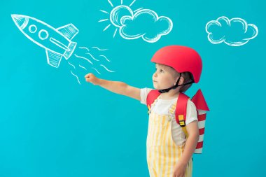 Mavi arka planda oyuncak kağıt kanatlarla oynayan mutlu çocuk. Çocuk evde eğleniyor. Hayal gücü, yaratıcı ve başlangıç konsepti