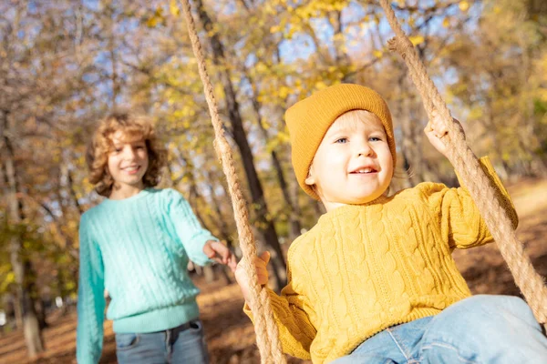 快乐的孩子们在秋天的公园里玩得很开心 孩子们在黄色模糊的树叶背景下荡秋千 自由和无忧无虑的概念 — 图库照片