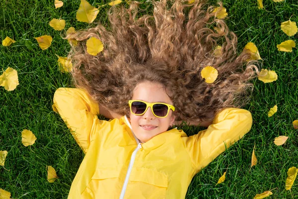 秋の公園に黄色の葉を持つ芝生の上に寝そべっている美しい女の子 楽しいアウトドアを持つ幸せな子供 — ストック写真