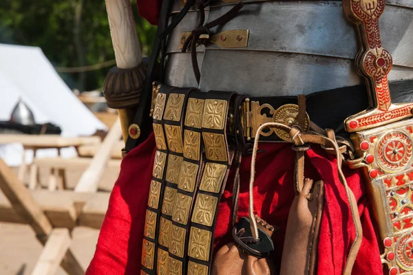 Details of ancient Roman soldier or legionary body armor. Metal body plates, leather belt with groin protection leather and metal stripes, decorated dagger, red wool tunic, leather bags and a sword.
