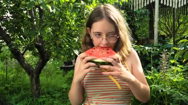 Jong meisje in glazen eet een watermeloen in de tuin — Stockvideo