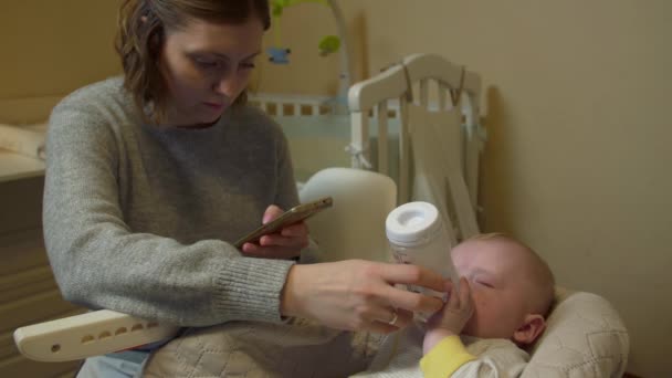 Мать кормит ребенка с помощью телефона — стоковое видео