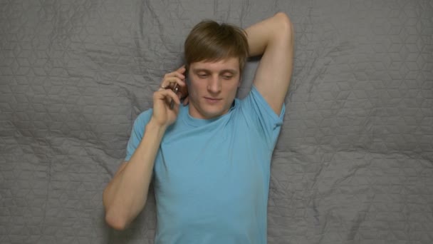 Genç adam konuşan telefon üzerinde yatak — Stok video