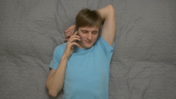 Молодой человек звонит по телефону на кровати — стоковое видео