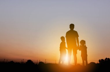 Gün batımında eğlenen baba ve iki çocuğun silueti. Mutlu aile kavramı..