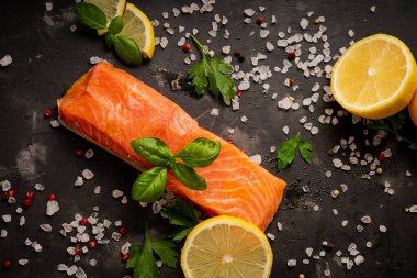 Baharatlı hafif tuzlu alabalık dilimleri, koyu bir masada fesleğen ve limon.