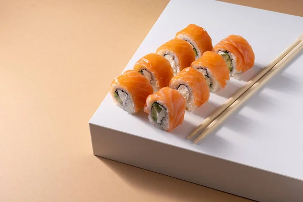 Seçici odak noktası, balık somonu ve krem peynirli bej renkli tek renkli arka plan ve Çin yemek çubuklarıyla Japon suşisi Philadelphia.