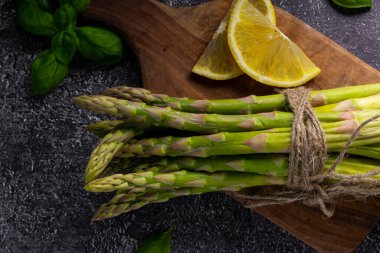 Seçici odak noktası, yeşil kuşkonmaz kapsülleri, koyu bir arka plan. Limon dilimleri, baharatlar ve fesleğenli.