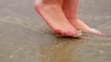 Kadınların ayakları kumlu sahilde yürür.