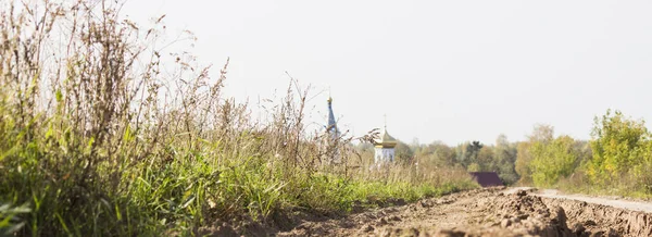 Road on a grass covered land with church steeple and rooftop background. Russian field.