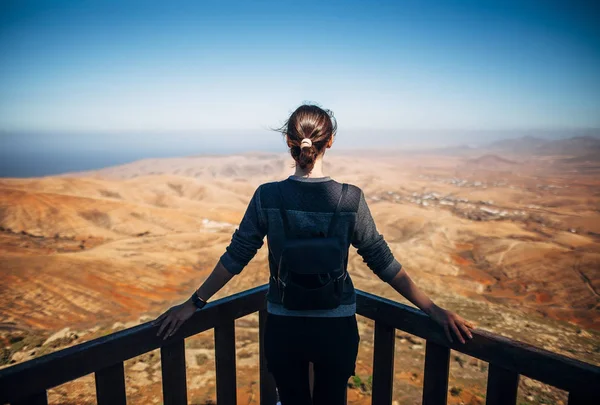 Woman looking at volcanic mountains and ocean landscape from Mirador de Morro Velosa viewpoint, Fuerteventura, Canary Islands, Spain.