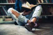 Fiatal tanuló ember ült a padlón, könyvet olvas, és pihentető könyvtár. A hangsúly a csizma