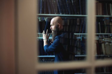 Kütüphane penceresinden kitaplık defterinden alarak sakallı adam. Eğitim kavramı