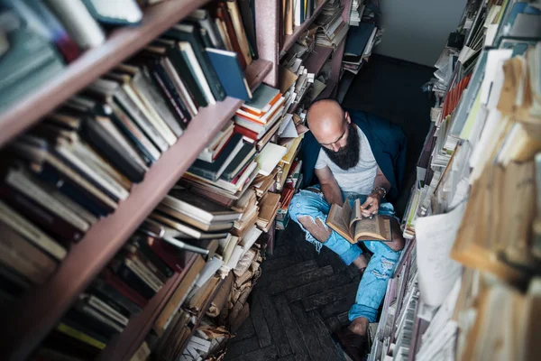 有胡子的年轻人看书坐在书架之间的地板上 顶部视图 放松和爱好概念 — 图库照片
