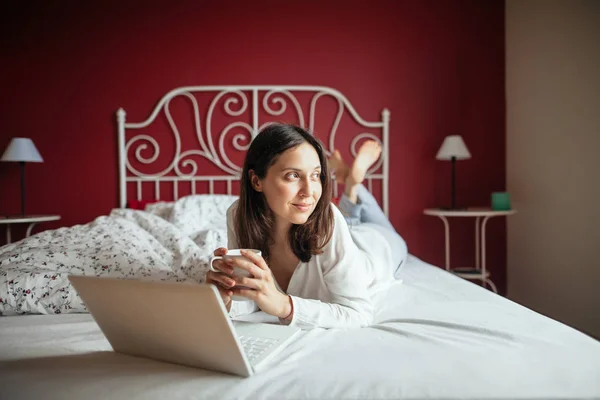 体贴的女人在床上放松 在家里用笔记本电脑喝咖啡 休息概念 — 图库照片
