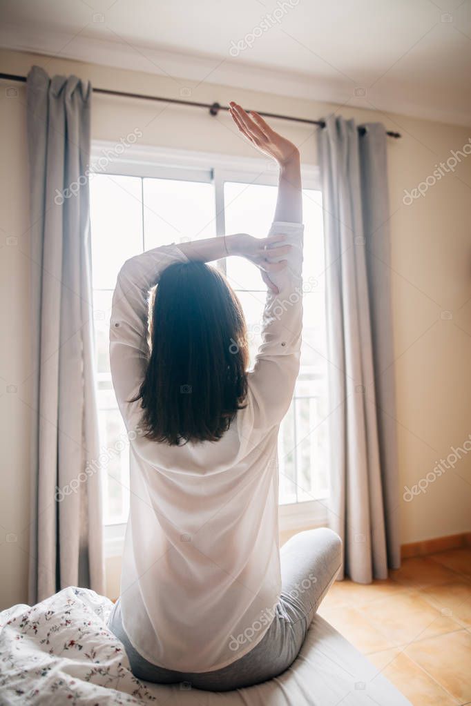 Pretty woman stretching in bed after wake up, back view