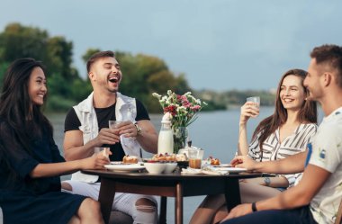 Yemek ve having fun nehir kıyısındaki restoranda genç arkadaşlar.