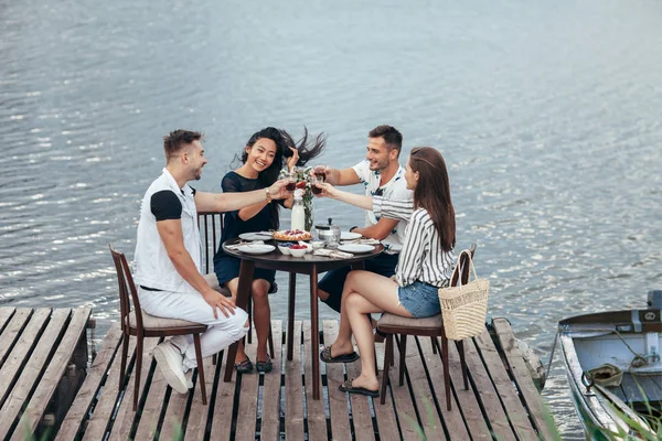 Grupo Jóvenes Amigos Comiendo Divirtiéndose Restaurante Aire Libre Junto Río —  Fotos de Stock