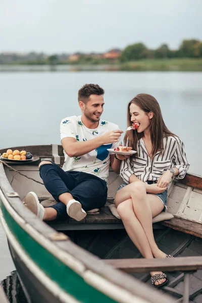 Romantic date. Lovers in boat on lake. Happy couple with relaxing on water with sweet fruits.