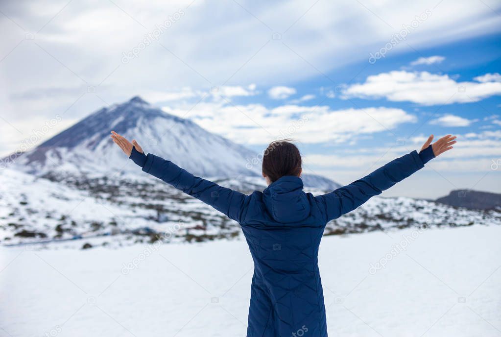 Back view of young happy woman with hands up enjoying snow mountains with volcano El Teide on background. Winter in Canary Islands
