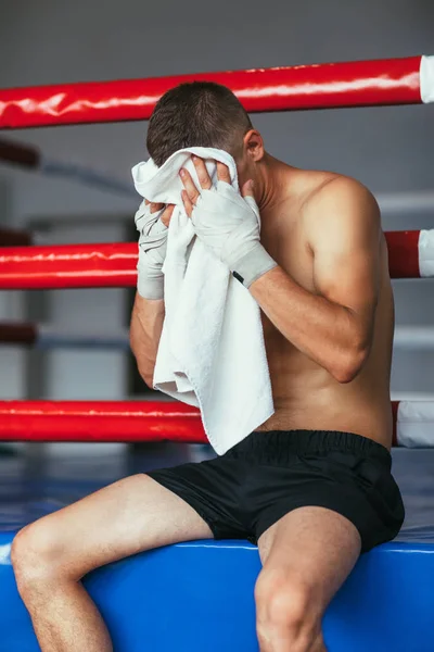 ボクサーはボクシングのリングで座っている堅い戦いの後タオルで汗を拭く — ストック写真