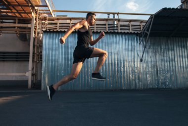 Arka bina ndustrial çalışan yakışıklı delikanlı. Runner, koşucu, fitness aktivitesi