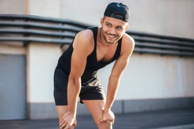 Runner rahatlatıcı egzersiz yaptıktan sonra gülümseyerek. Elleriyle çalıştırdıktan sonra diz dinlenme dinlenme alarak atlet