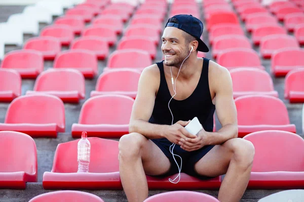 微笑的运动的人在耳机听音乐坐在体育场座位上 — 图库照片