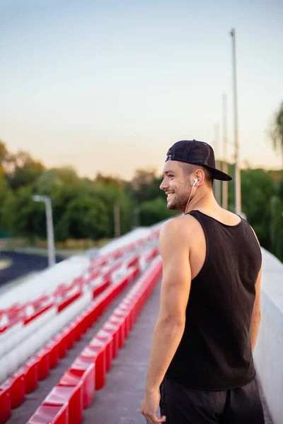 英俊的微笑的人在耳机听音乐在体育场背景 — 图库照片