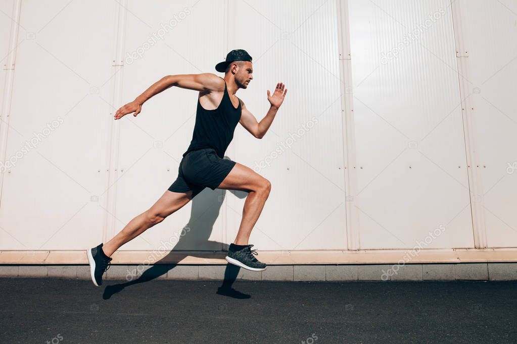 Young man runner running along wall with copy space. Sport, fitness, jogging