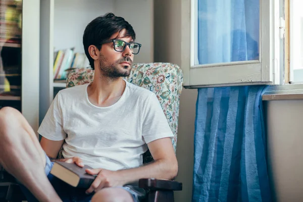 Genç Düşünceli Adam Rahat Sandalyede Evde Kitap Ile Geri Kalan — Stok fotoğraf