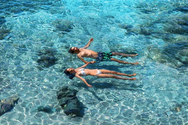 幸せなカップルは 透明なターコイズ ブルーの海で泳いで 熱帯の休暇や新婚旅行のコンセプトです 平面図 — ストック写真