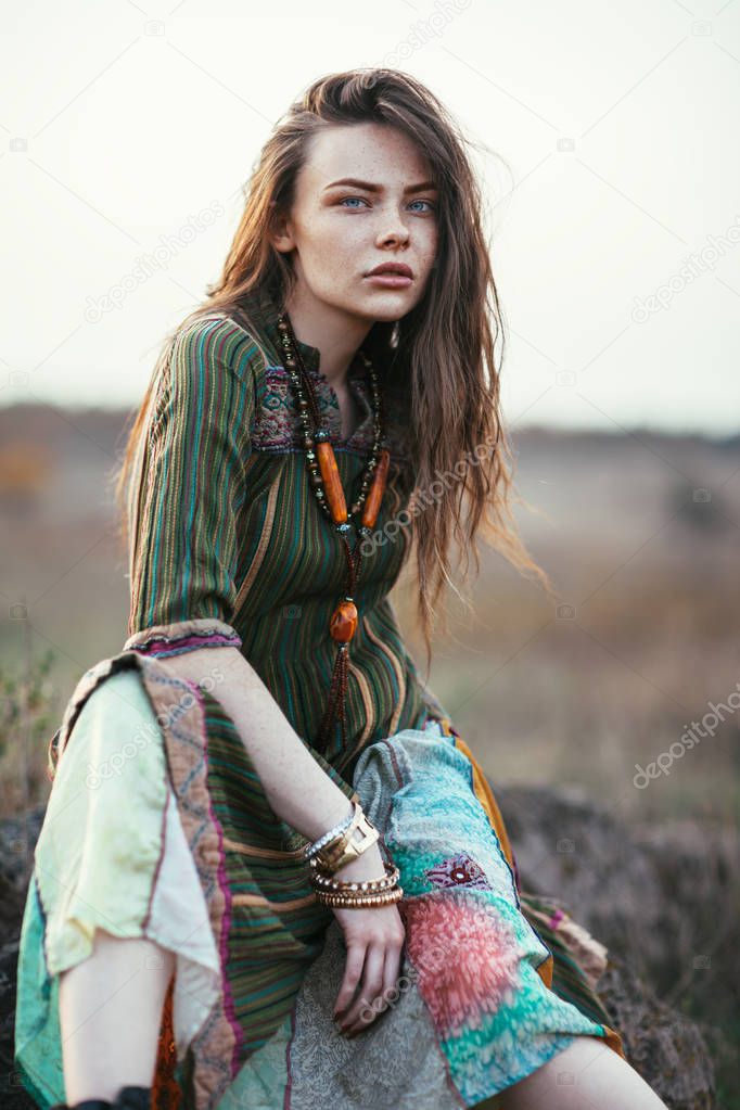 Fashion portrait of young hippie woman at sunset posing on nature background