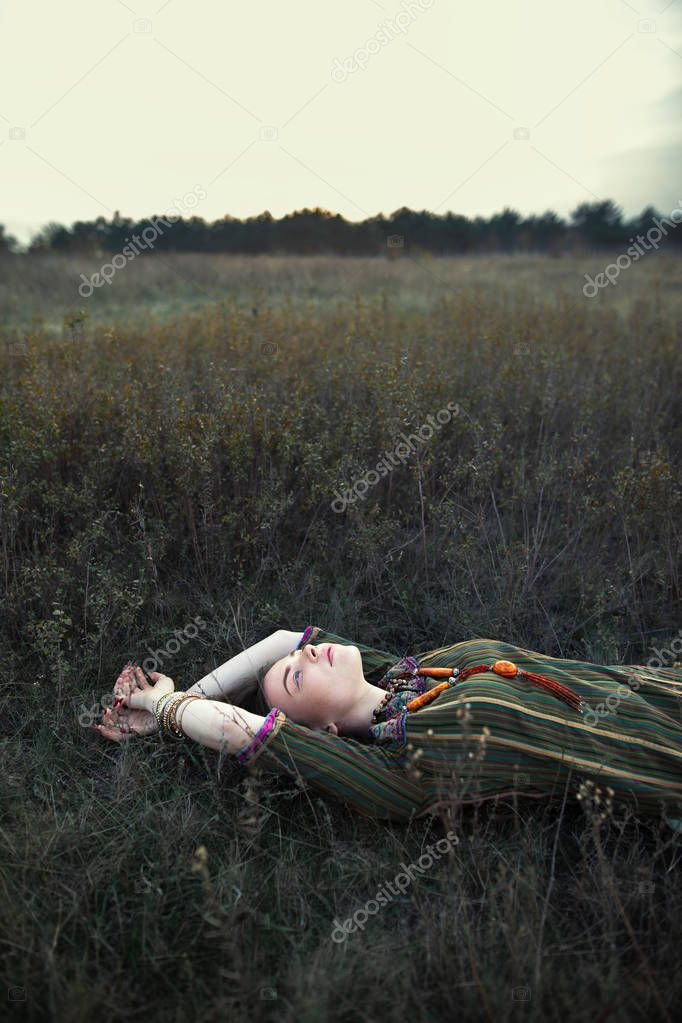 Beautiful hippie woman lying on grass relaxing on summer field. Carefree concept