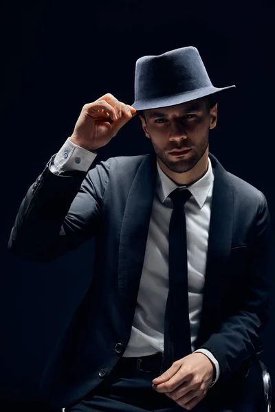 黒のスーツの若いハンサムな男は暗い背景に彼の帽子に触れる 男の美しさ挨拶の概念 — ストック写真