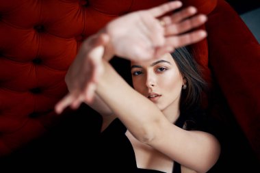 Şehvetli güzel kadın portre kırmızı kanepe üzerinde seksi siyah elbise poz bir el çerçevesi ile bakıyor. Kadın güzellik ve moda konsepti                               