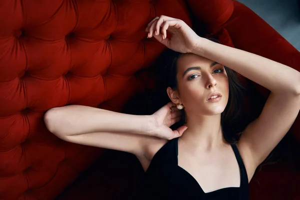 赤いソファにセクシーな黒いドレスでポーズをとる官能的な美しい女性 女性の美しさの概念 — ストック写真