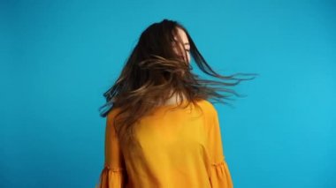 Mavi arka plan üzerinde yavaş çekimde uzun saçlı başını sallayarak güzel genç kadın 