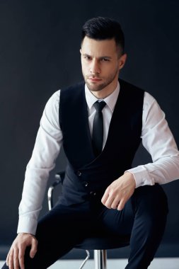 Yakışıklı kendine güvenen adam portre sandalyede oturan ve siyah arka plan üzerinde poz